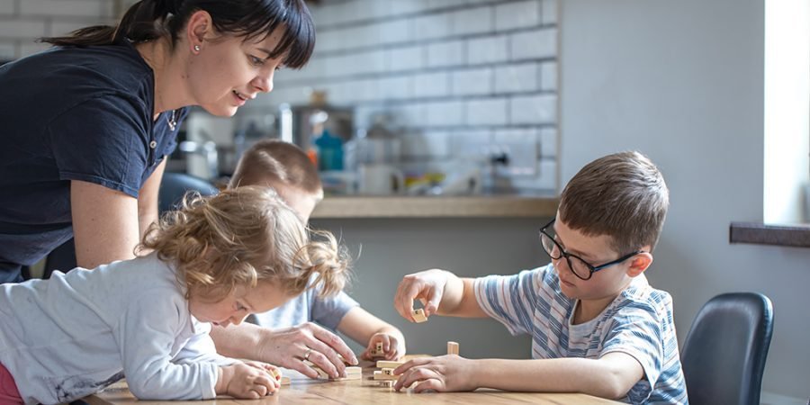 Children with their mother play board at home in the kitchen.